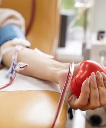 Close-up of patient with tubes in her arm squeezing the ball in her hand while donating the blood
